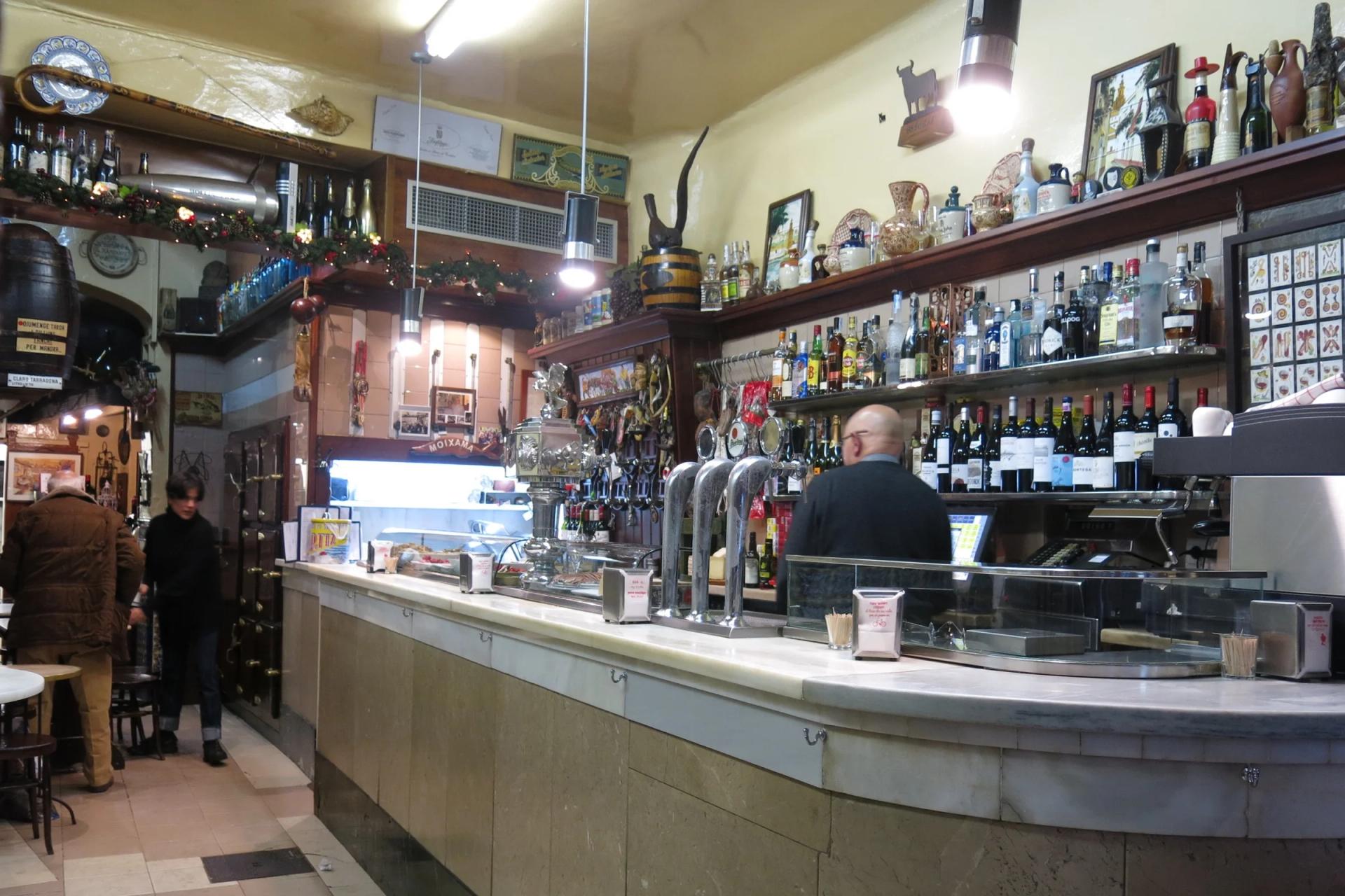 Barra de mármol de El Xampanyet, con botellas y azulejos en las paredes