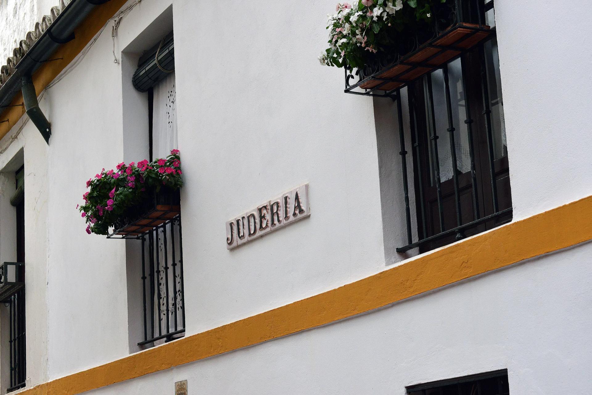 Placa de la calle Judería sobre una fachada encalada con macetas
