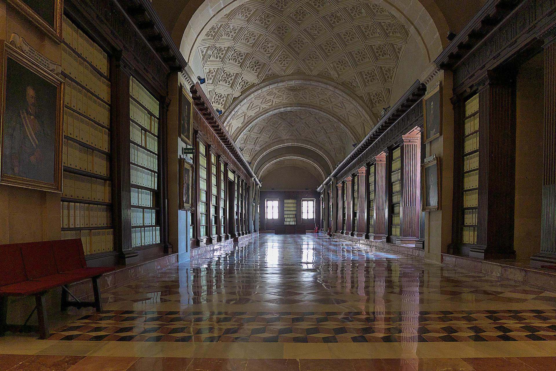 Galería del piso superior del Archivo de Indias, con estanterías de madera y suelo de mármol