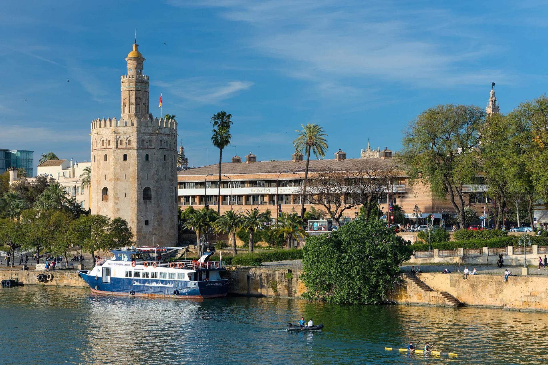 La Torre del Oro junto al Guadalquivir, con un barco de paseo amarrado en la orilla