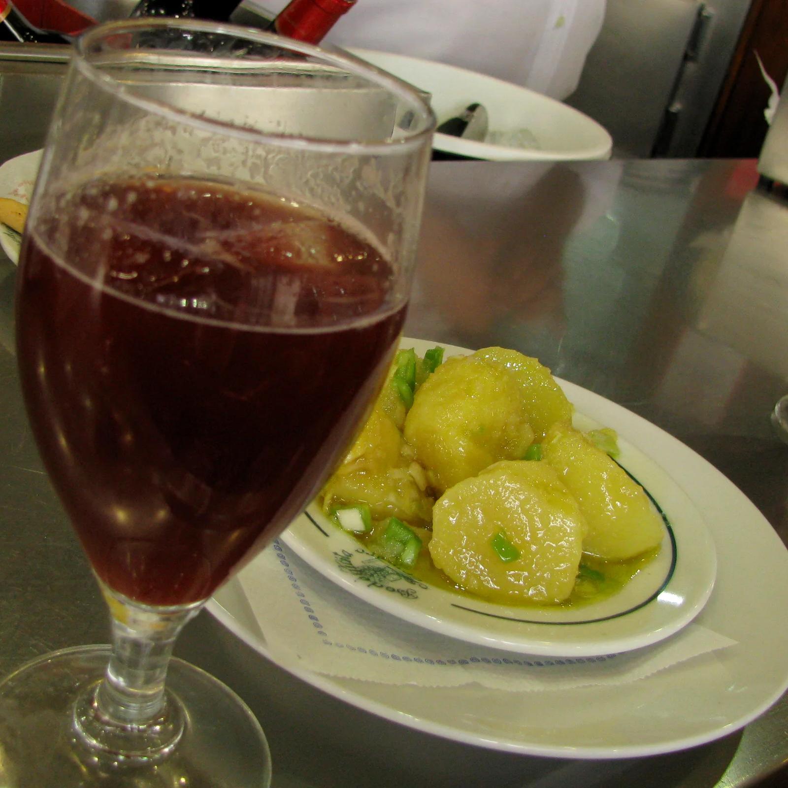Tapa de papas aliñás junto a una copa de vino tinto