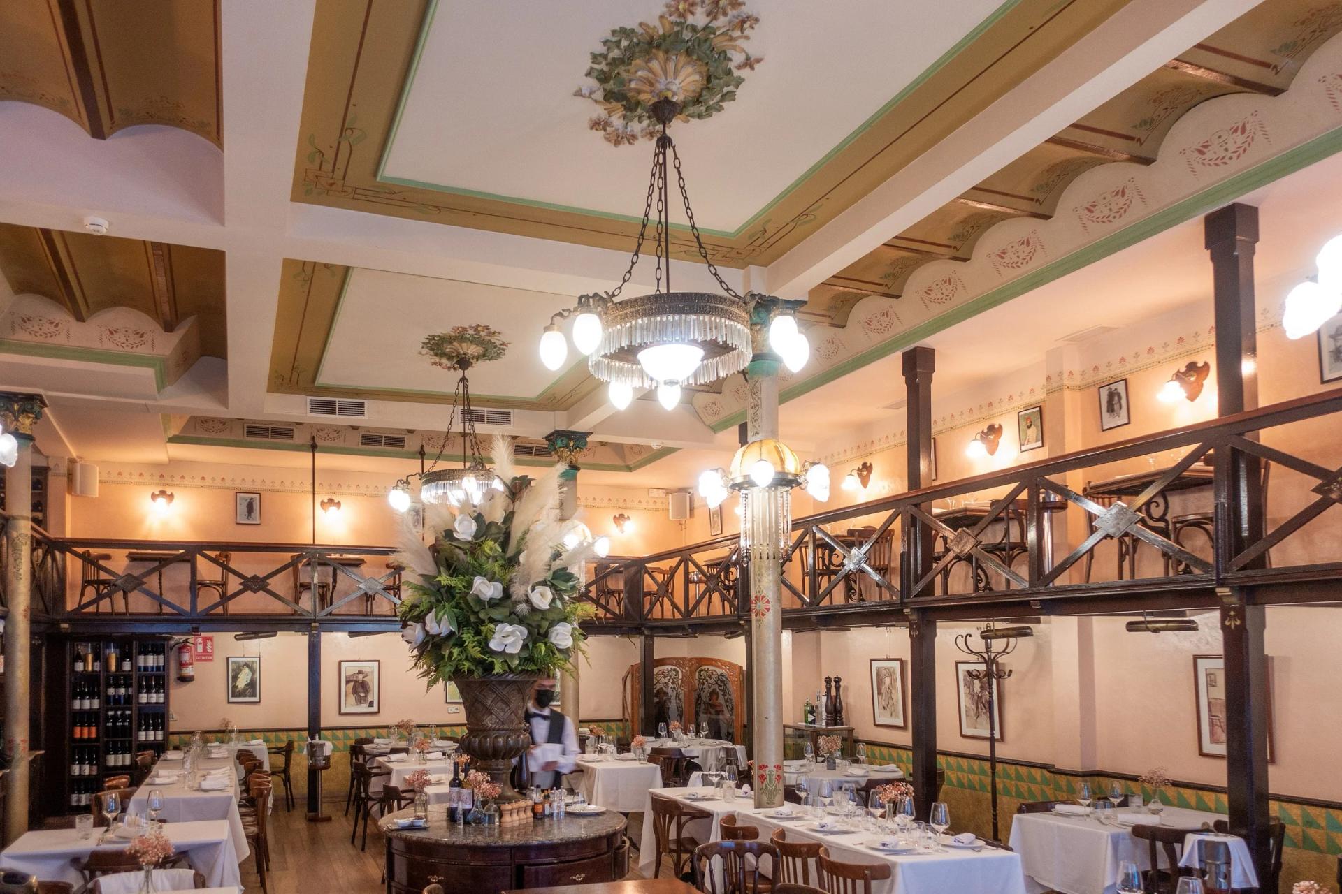Comedor de Els Quatre Gats, con lámparas de hierro, vigas de madera y cuadros en las paredes