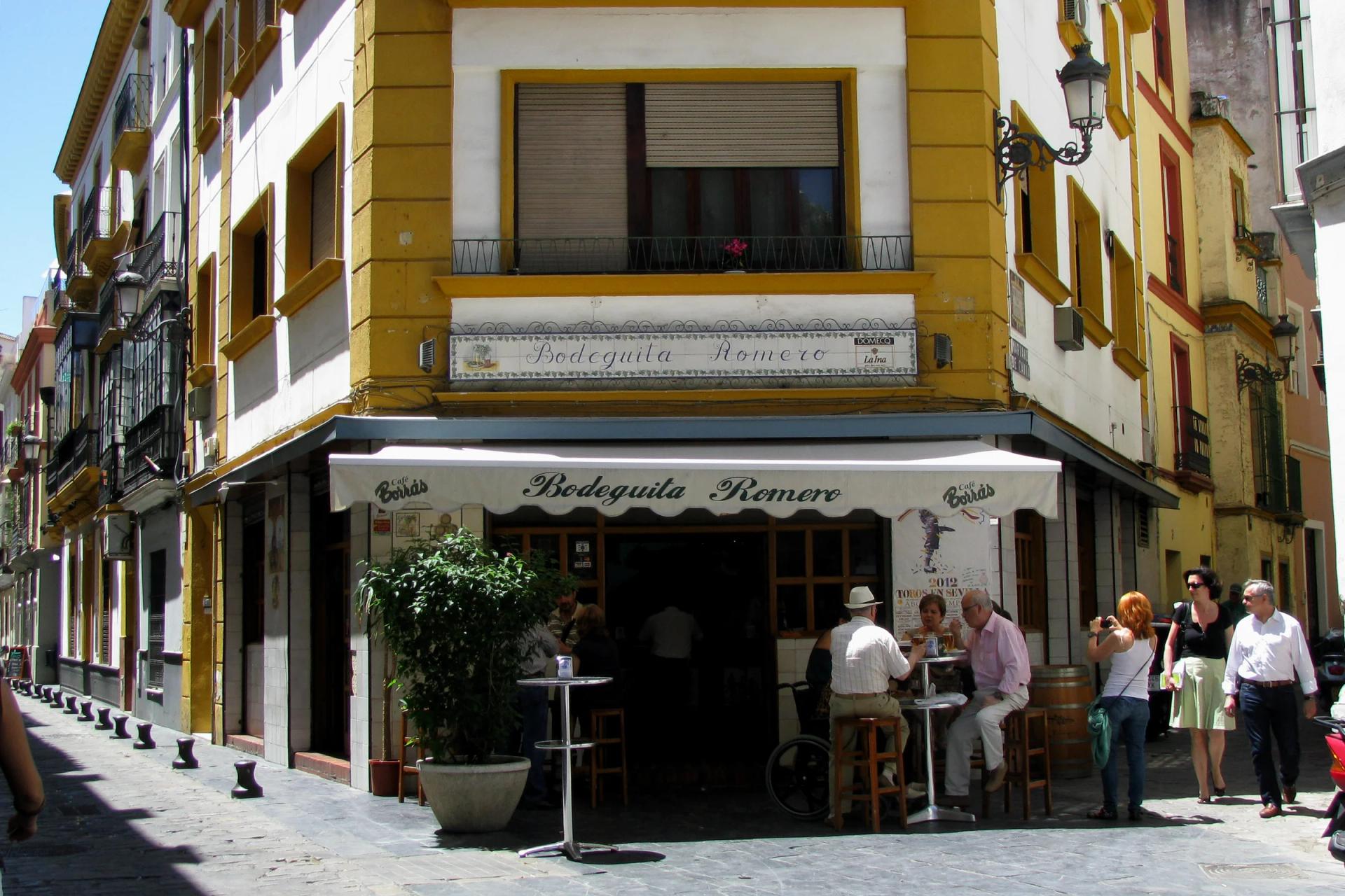 Fachada de la Bodeguita Romero en la calle Harinas, con gente tomando algo en la puerta